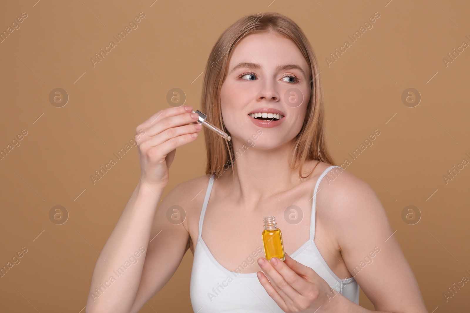 Photo of Beautiful young woman with bottle of essential oil on brown background