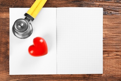 Photo of Stethoscope, open copybook and red heart on wooden background. Heart attack concept