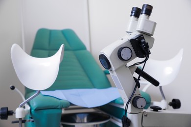 Modern binocular colposcope near gynecological chair in clinic