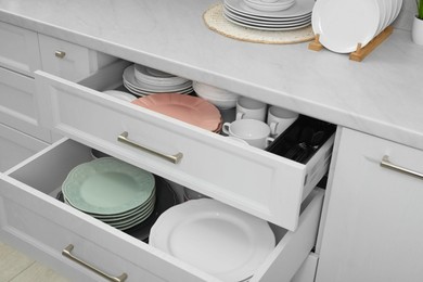 Photo of Clean plates and bowls in drawers indoors