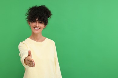 Photo of Happy young woman welcoming and offering handshake on green background, space for text