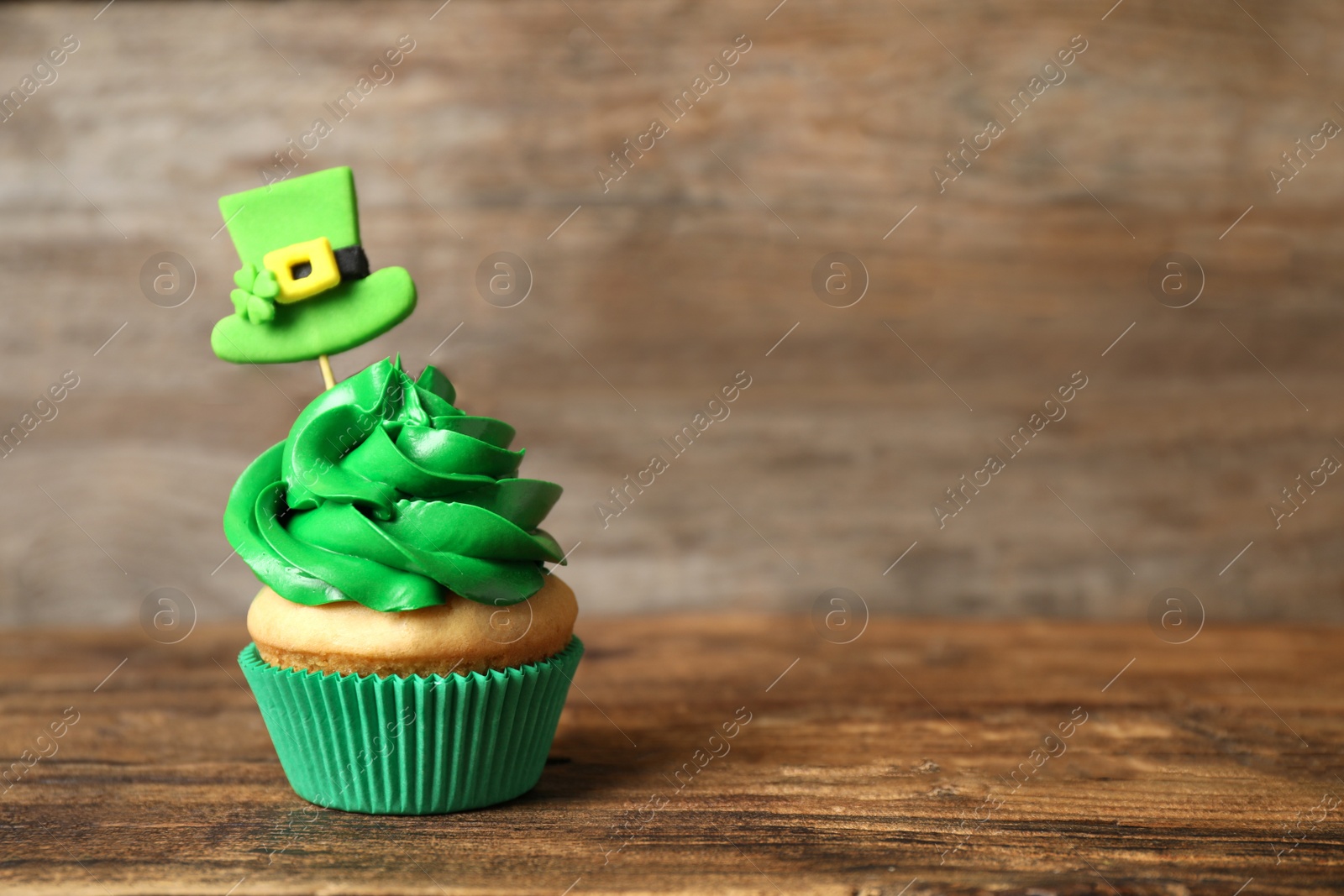 Photo of Decorated cupcake on wooden table, space for text. St. Patrick's Day celebration