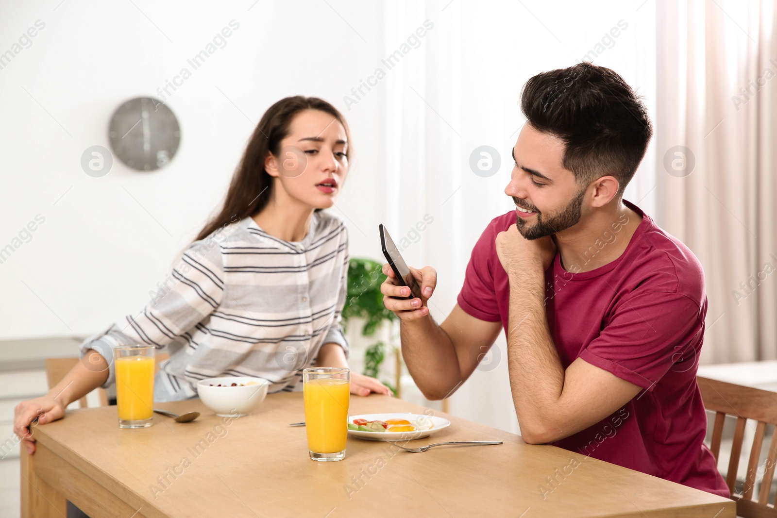 Photo of Distrustful young woman peering into boyfriend's smartphone at home