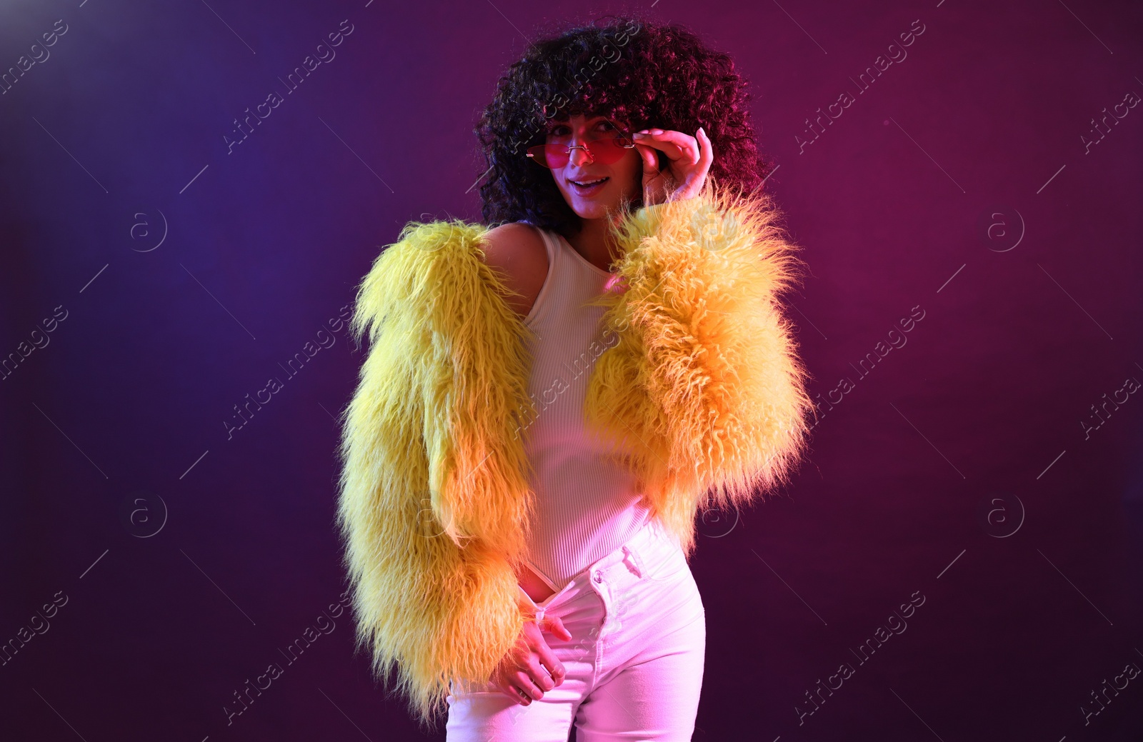 Photo of Beautiful young woman in yellow fur coat and sunglasses on color background in neon lights