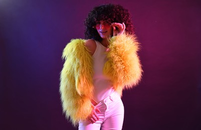 Photo of Beautiful young woman in yellow fur coat and sunglasses on color background in neon lights