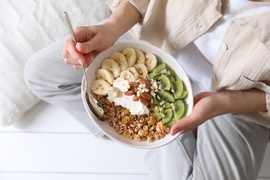 Photo of Woman eating tasty granola indoors, top view