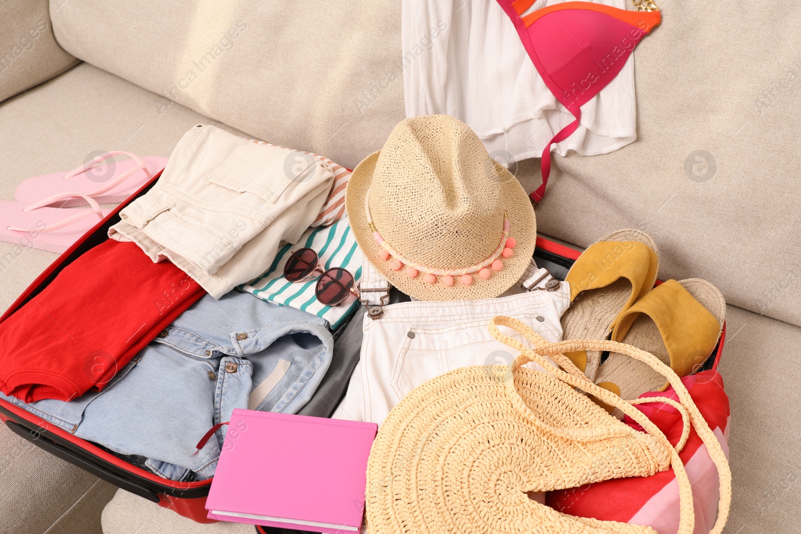 Photo of Open suitcase with different women clothes and accessories on sofa