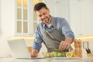 Photo of Man making dinner while watching online cooking course via laptop kitchen