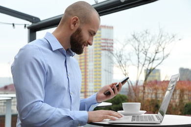 Businessman with laptop and mobile phone in outdoor cafe. Corporate blog