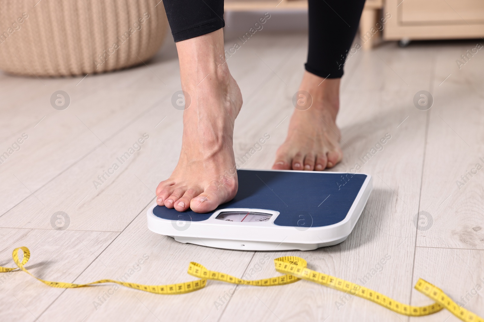 Photo of Woman stepping on floor scale and measuring tape at home, closeup. Weight control