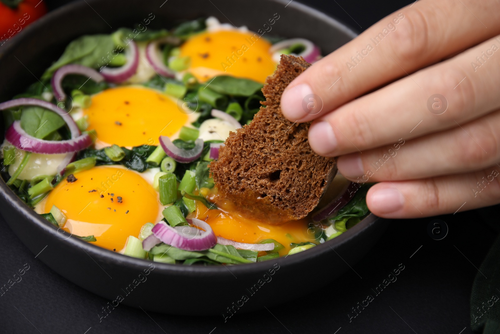 Photo of Woman dipping piece of bread into egg yolk, closeup. Eating tasty Shakshuka