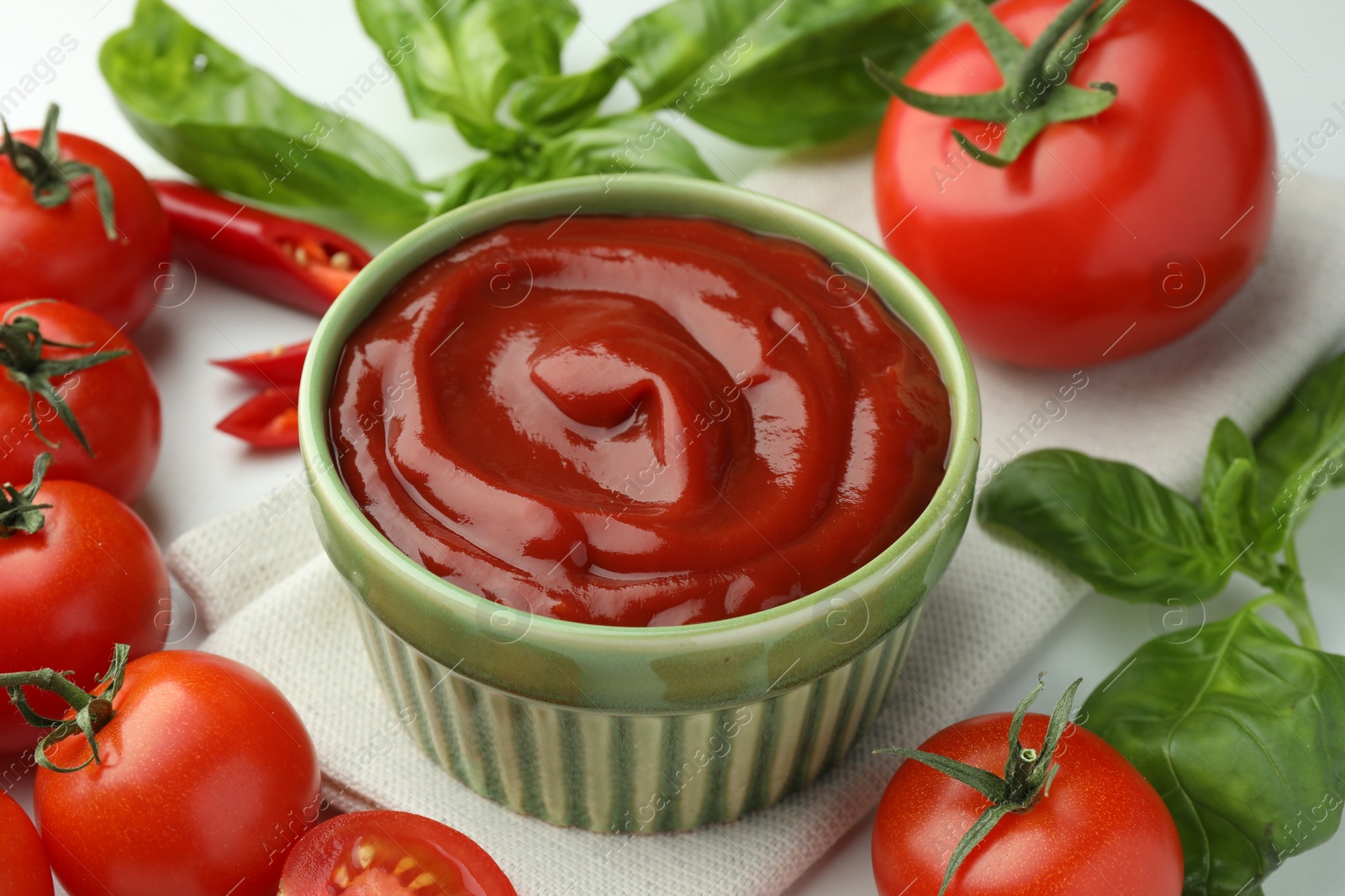 Photo of Bowl of tasty ketchup and ingredients on white table, closeup