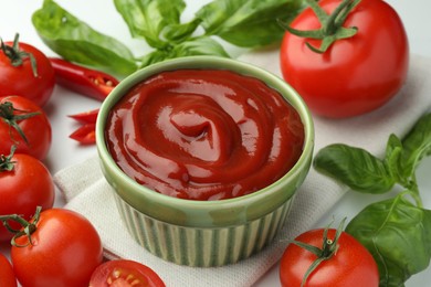 Photo of Bowl of tasty ketchup and ingredients on white table, closeup