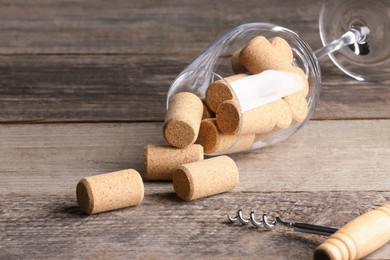 Glass with wine corks and corkscrew on wooden table