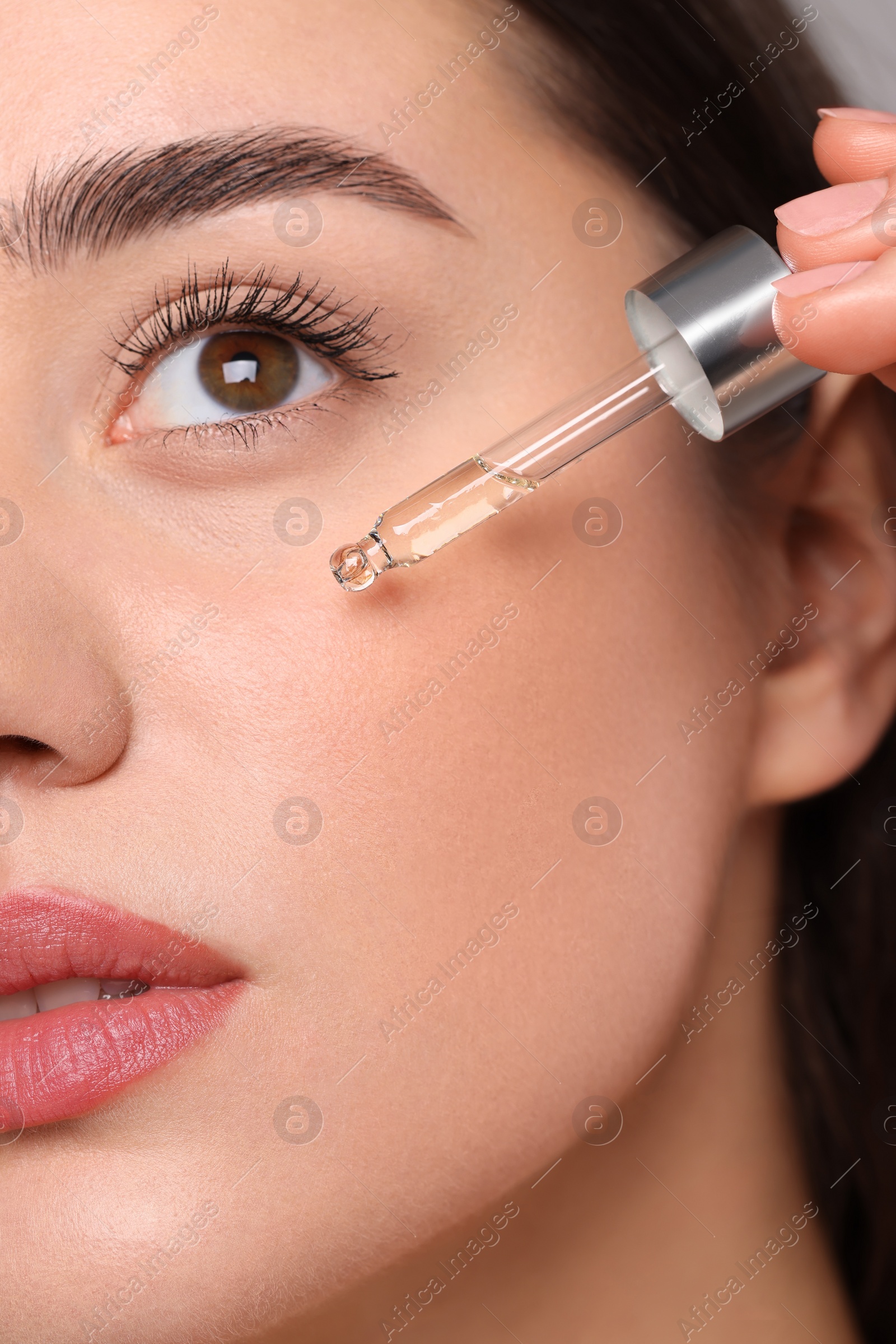 Photo of Young woman applying essential oil onto face, closeup