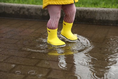 Girl walking in puddle outdoors on rainy weather, closeup
