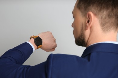 Businessman looking at wristwatch on grey background. Time management