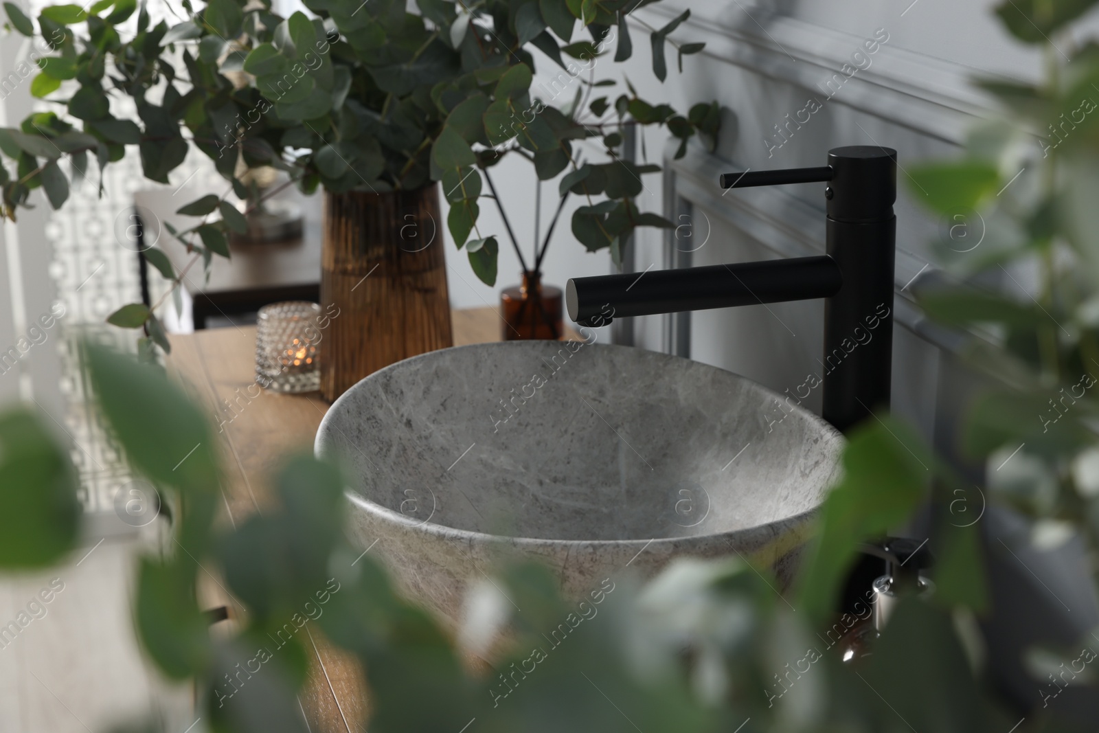 Photo of Eucalyptus branches near vessel sink on bathroom vanity. Interior design