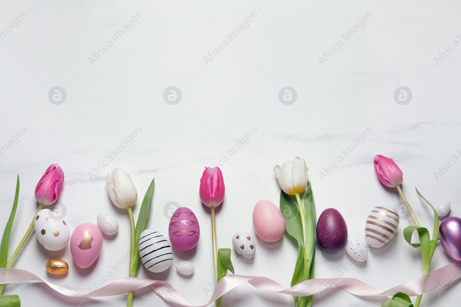 Photo of Flat lay composition of painted Easter eggs and tulip flowers on white marble table. Space for text