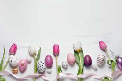 Flat lay composition of painted Easter eggs and tulip flowers on white marble table. Space for text