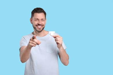 Photo of Happy man holding condom on light blue background. Space for text