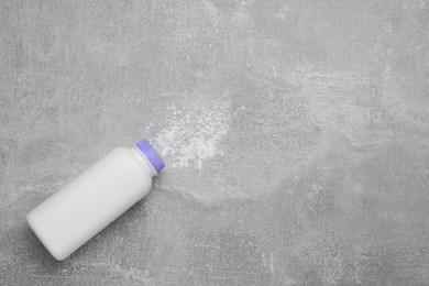 Bottle and scattered baby powder on grey table, top view with space for text