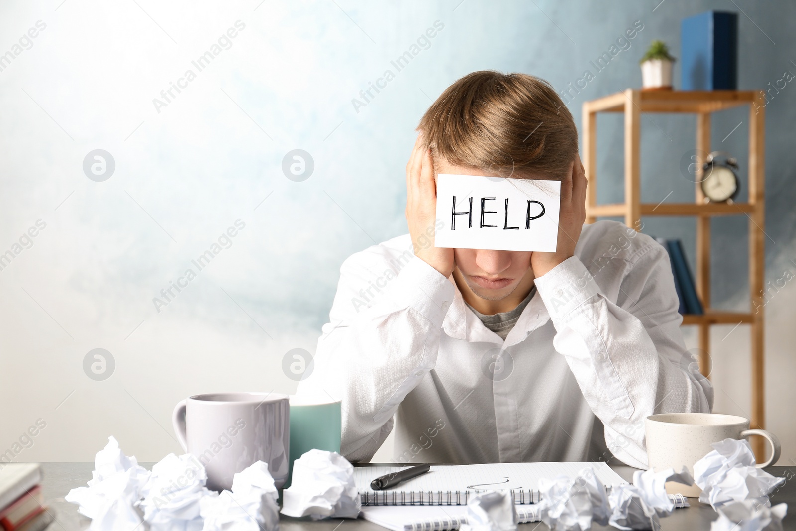 Photo of Young man with note HELP on forehead at workplace. Space for text