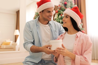 Happy couple in Santa hats with Christmas gift at home