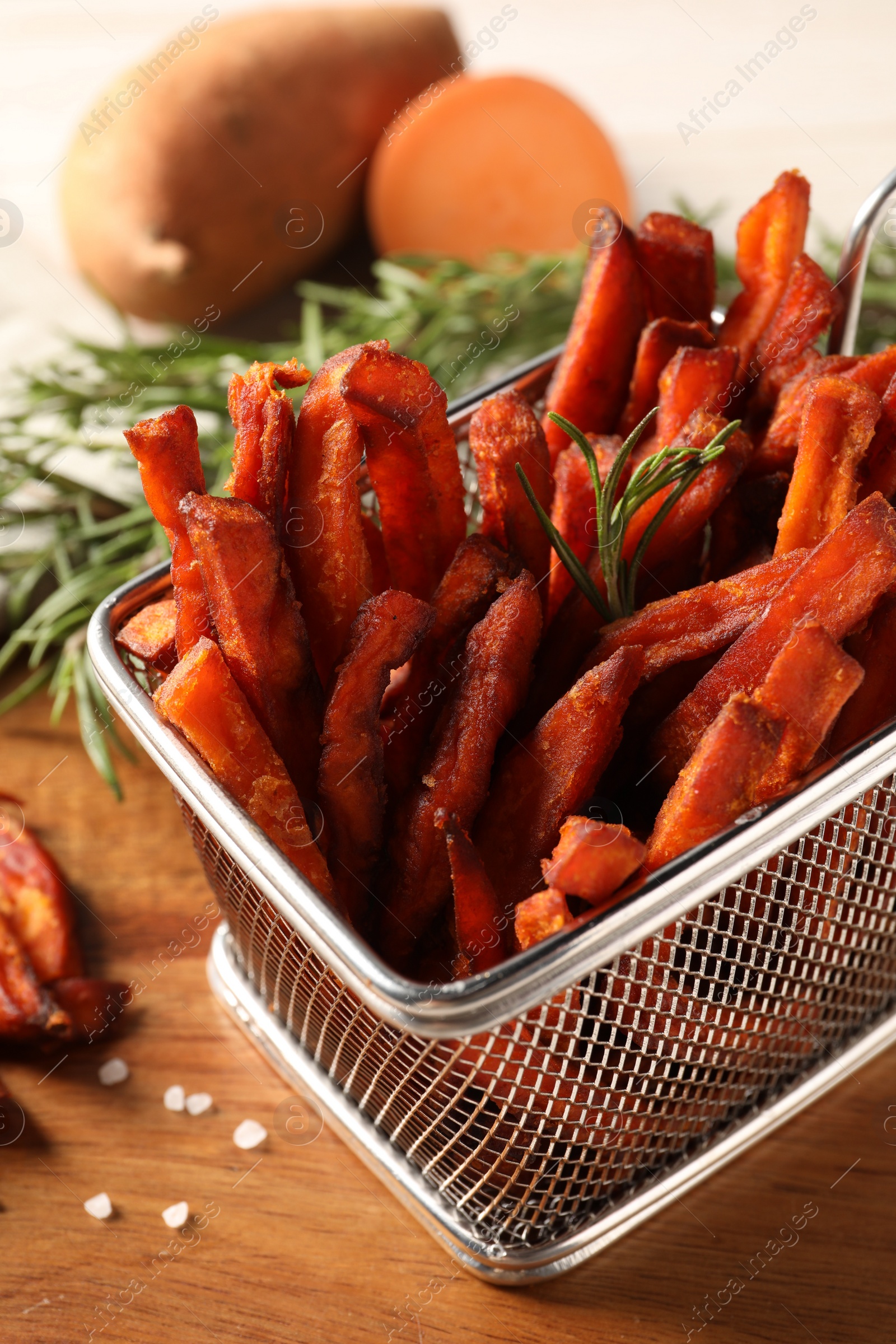 Photo of Frying basket with sweet potato fries and rosemary on wooden table, closeup