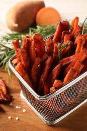 Photo of Frying basket with sweet potato fries and rosemary on wooden table, closeup