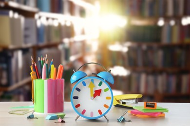 Light blue alarm clock and different stationery on white table in library