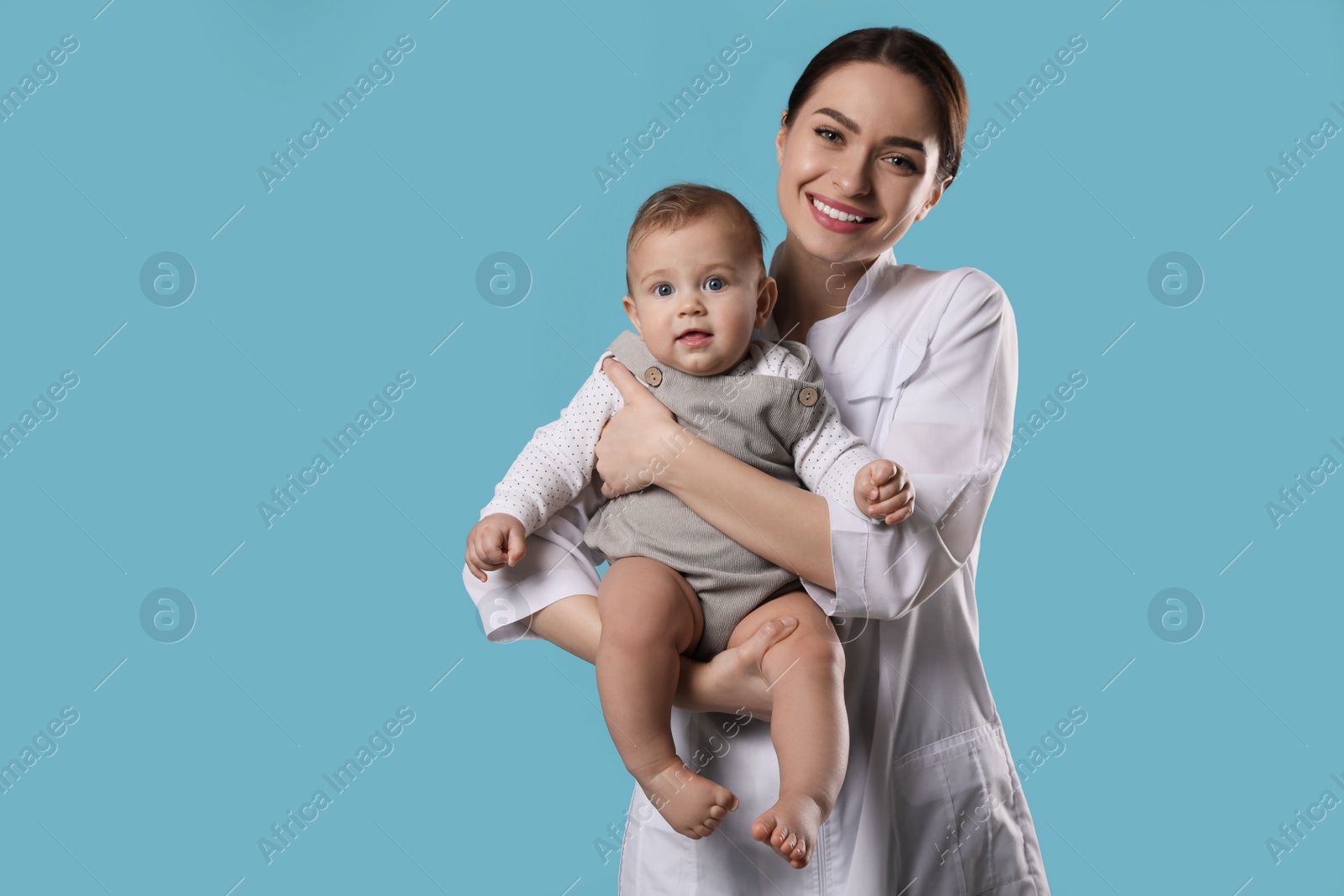 Photo of Young pediatrician with cute little baby on light blue background. Space for text