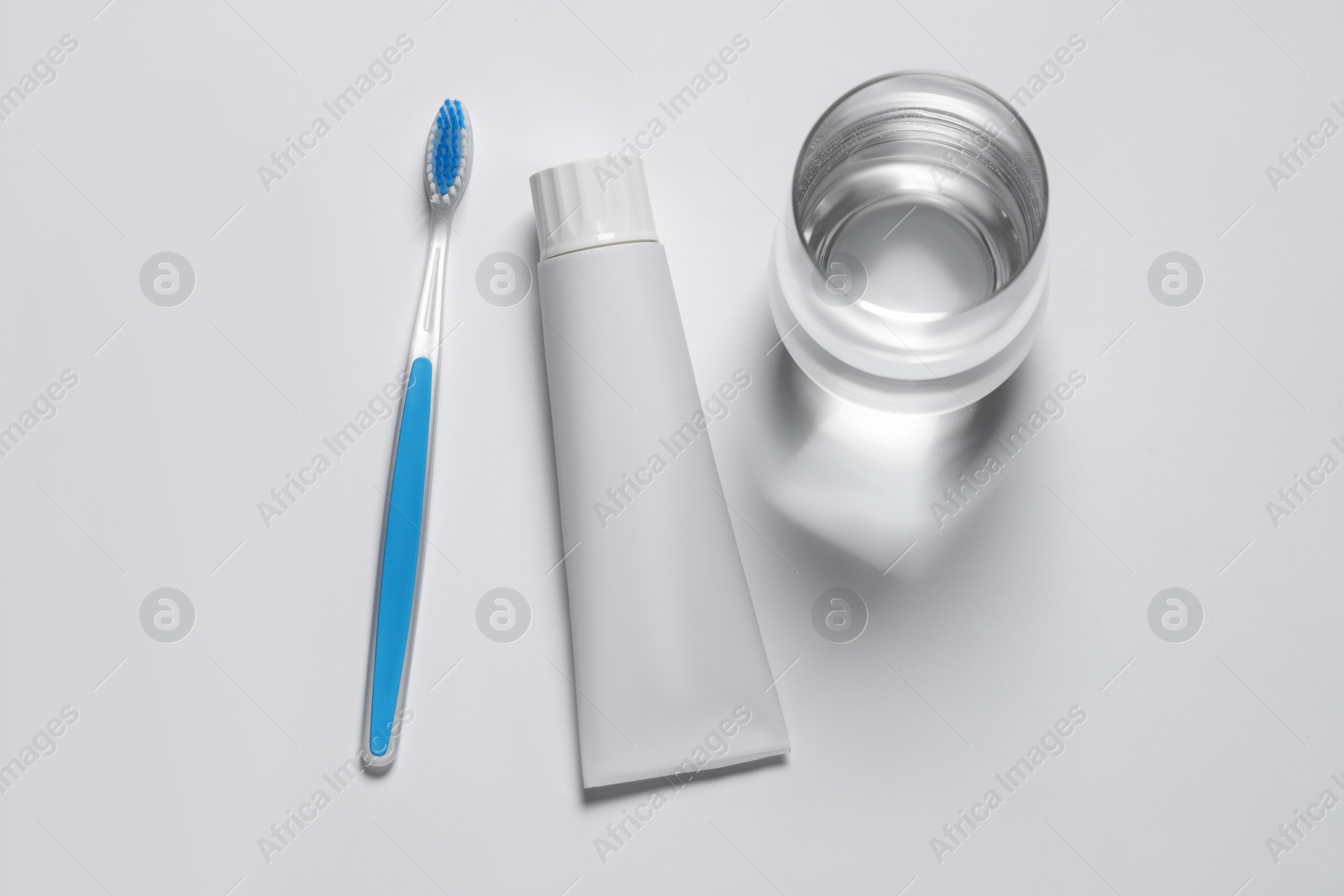 Photo of Plastic toothbrush with paste and glass of water on white background, top view