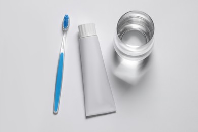 Photo of Plastic toothbrush with paste and glass of water on white background, top view