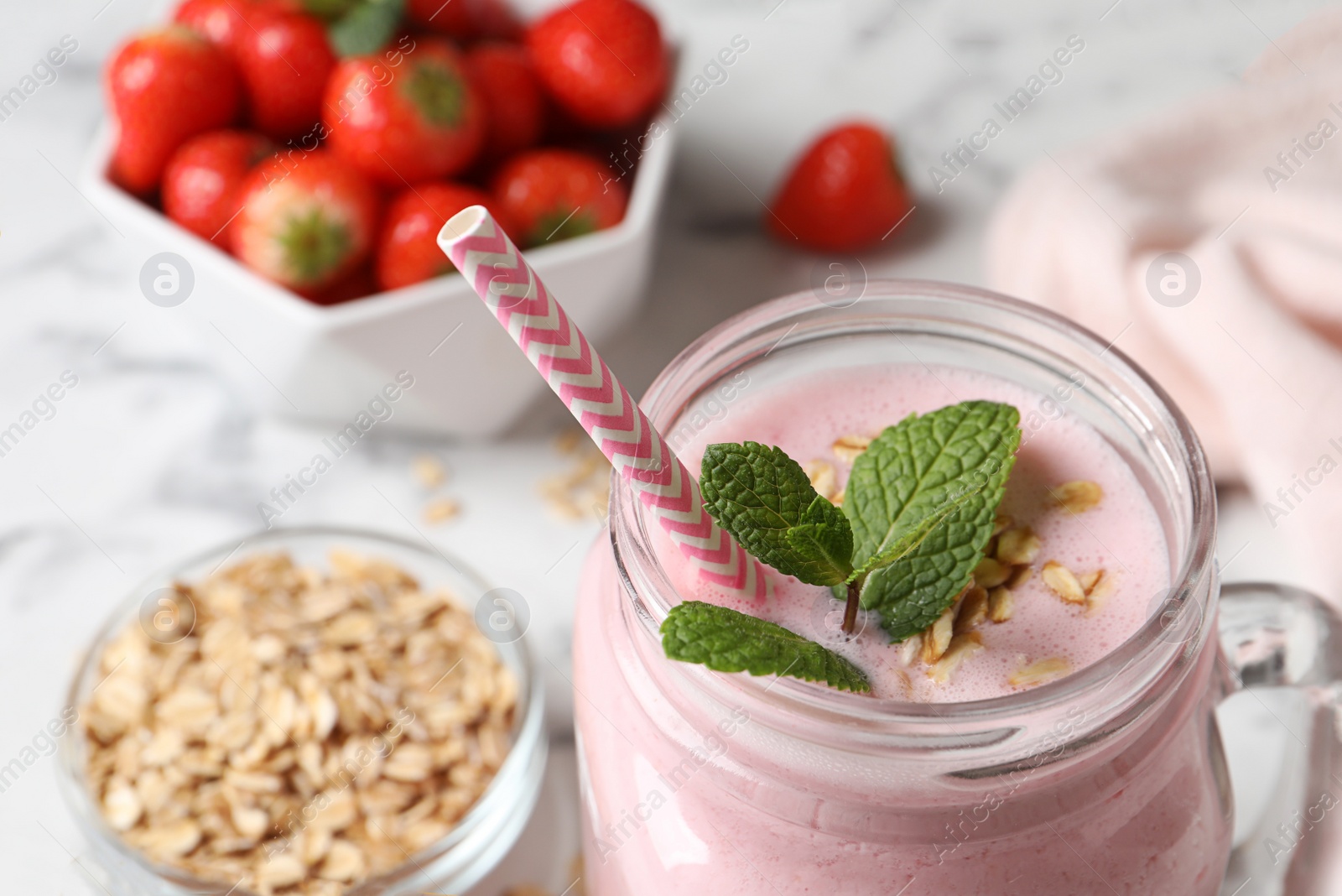 Photo of Mason jar of tasty strawberry smoothie with oatmeal and mint on white table, closeup