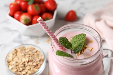 Photo of Mason jar of tasty strawberry smoothie with oatmeal and mint on white table, closeup