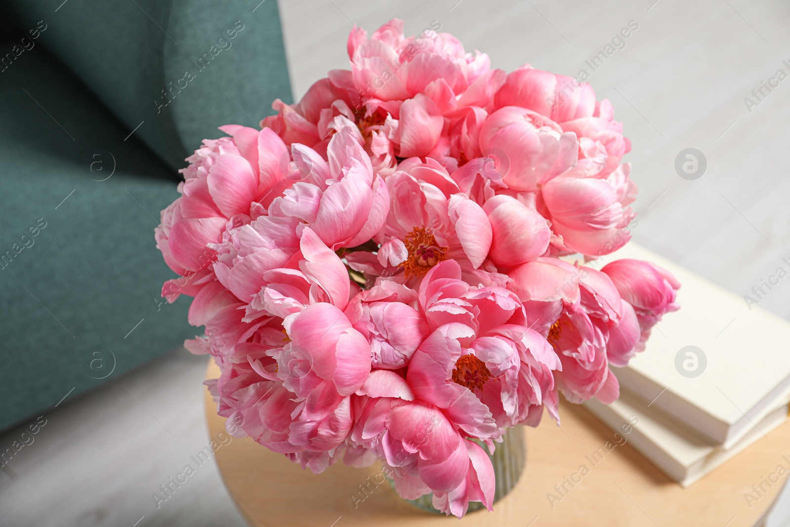 Photo of Beautiful bouquet of pink peonies in vase and books on wooden table indoors