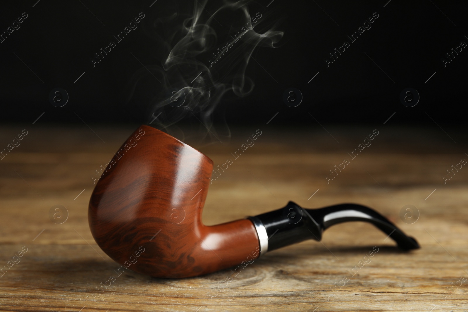 Photo of Classic stylish smoking pipe on wooden table, closeup