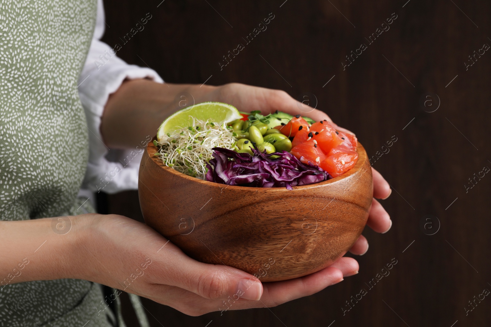 Photo of Woman holding delicious poke bowl with vegetables, fish and edamame beans on dark background, closeup