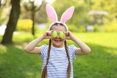 Photo of Easter celebration. Cute little girl in bunny ears covering eyes with painted eggs outdoors