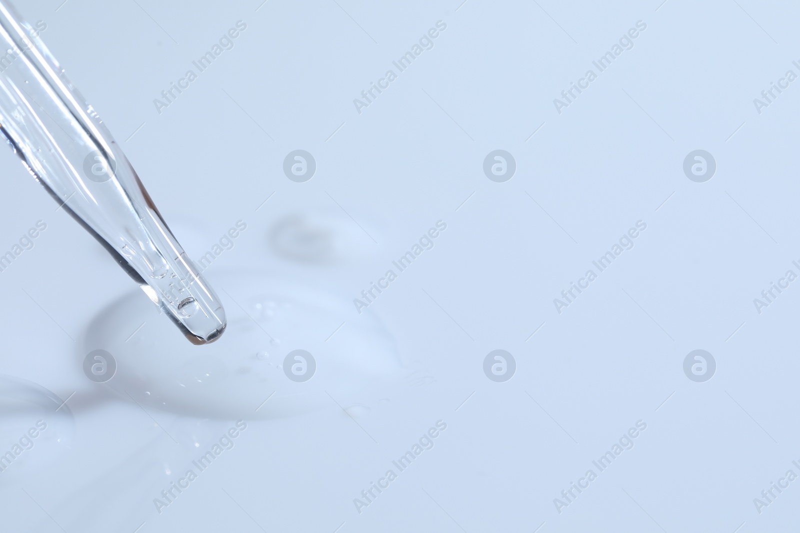 Photo of Glass pipette and transparent liquid on white background, closeup. Space for text