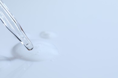 Photo of Glass pipette and transparent liquid on white background, closeup. Space for text