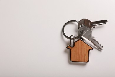 Photo of Keys with trinket in shape of house on white background, top view and space for text. Real estate agent services