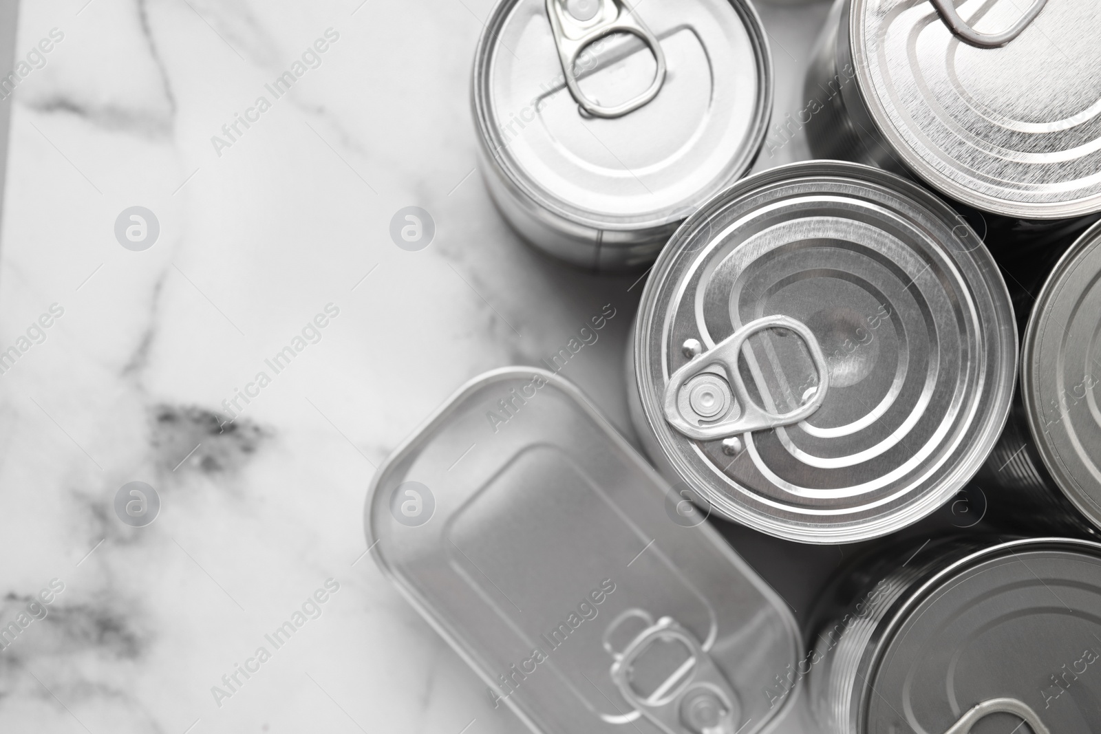 Photo of Many closed tin cans on white marble table, flat lay. Space for text