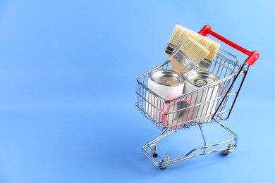 Photo of Small shopping cart with set of painting tools on light blue background. Space for text