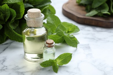 Photo of Bottle of mint essential oil and green leaves on white marble table, space for text