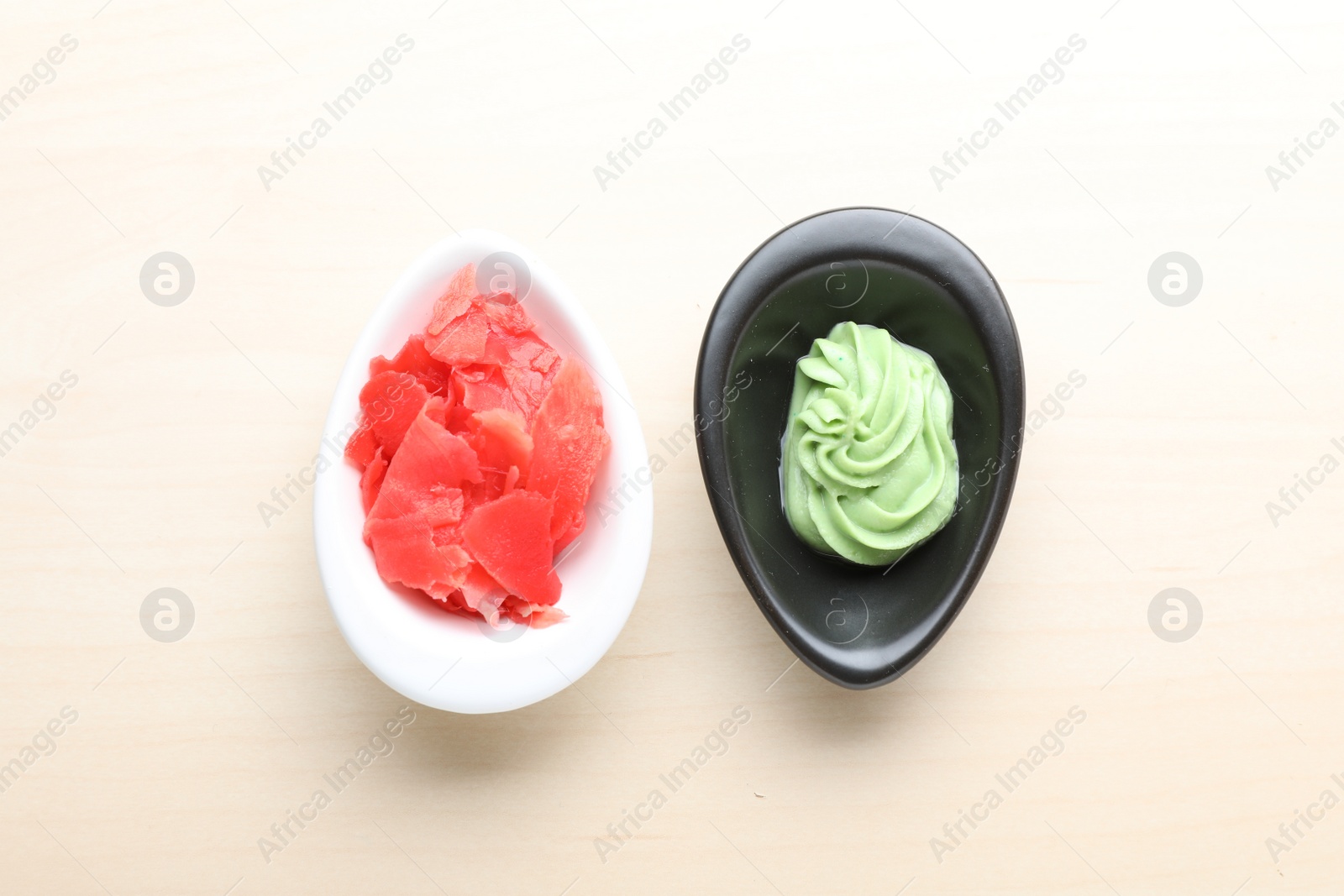 Photo of Bowls with swirl of wasabi paste and pickled ginger on white table, flat lay