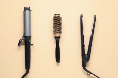 Photo of Curling iron, hair straightener and round brush on beige background, flat lay