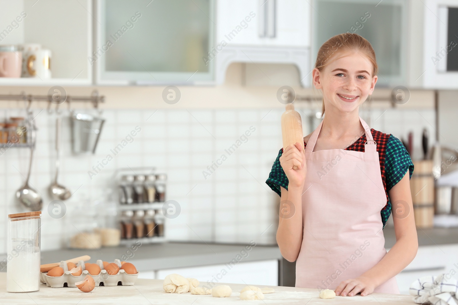 Photo of Teenage girl with rolling pin and raw dough in kitchen