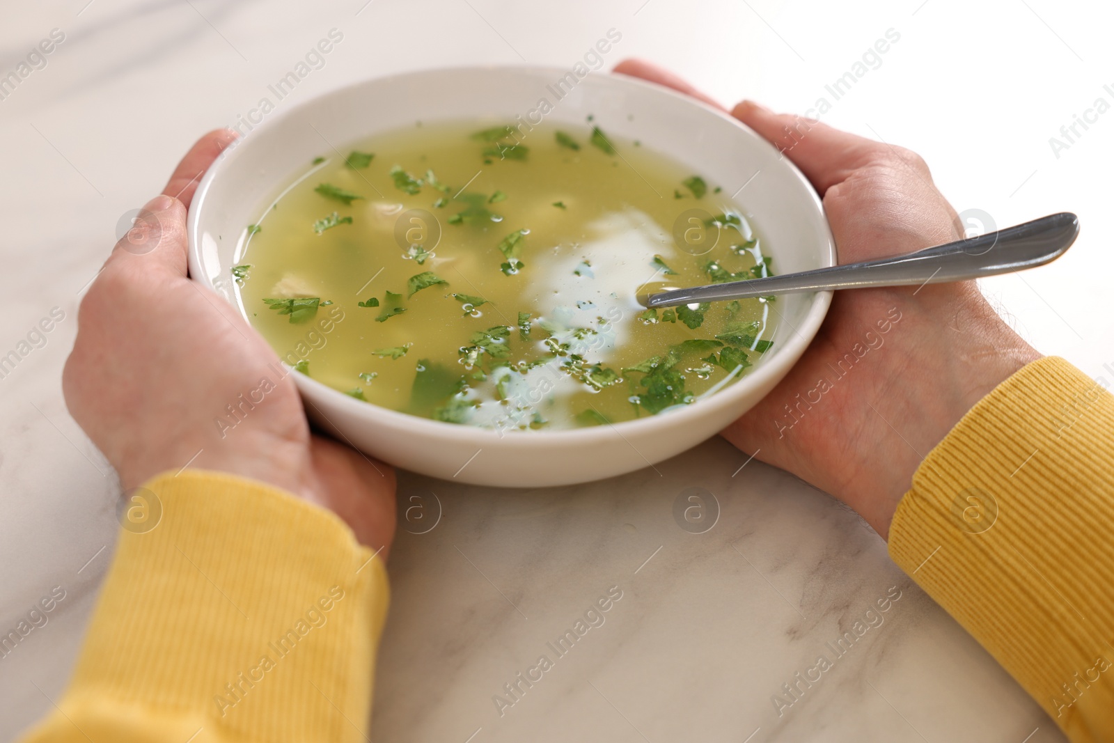 Photo of Man with bowl of delicious chicken soup at light marble table, closeup